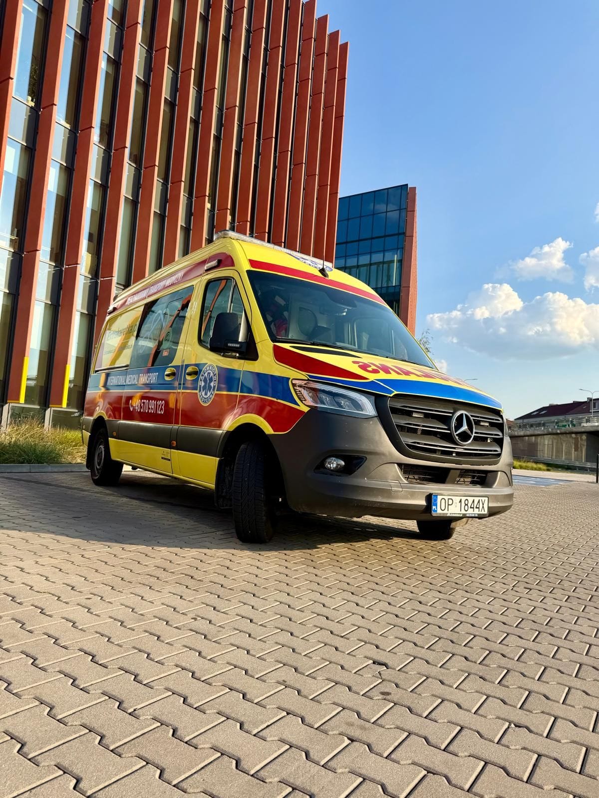 Ambulans Mercedes Sprinter Extrakaretka.pl do transportu medycznego, zaparkowany przed nowoczesnym biurowcem