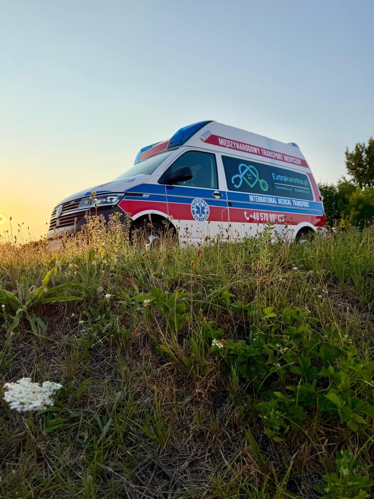 Ambulans Volkswagen Extrakaretka.pl z napisem „Międzynarodowy transport medyczny” o zachodzie słońca